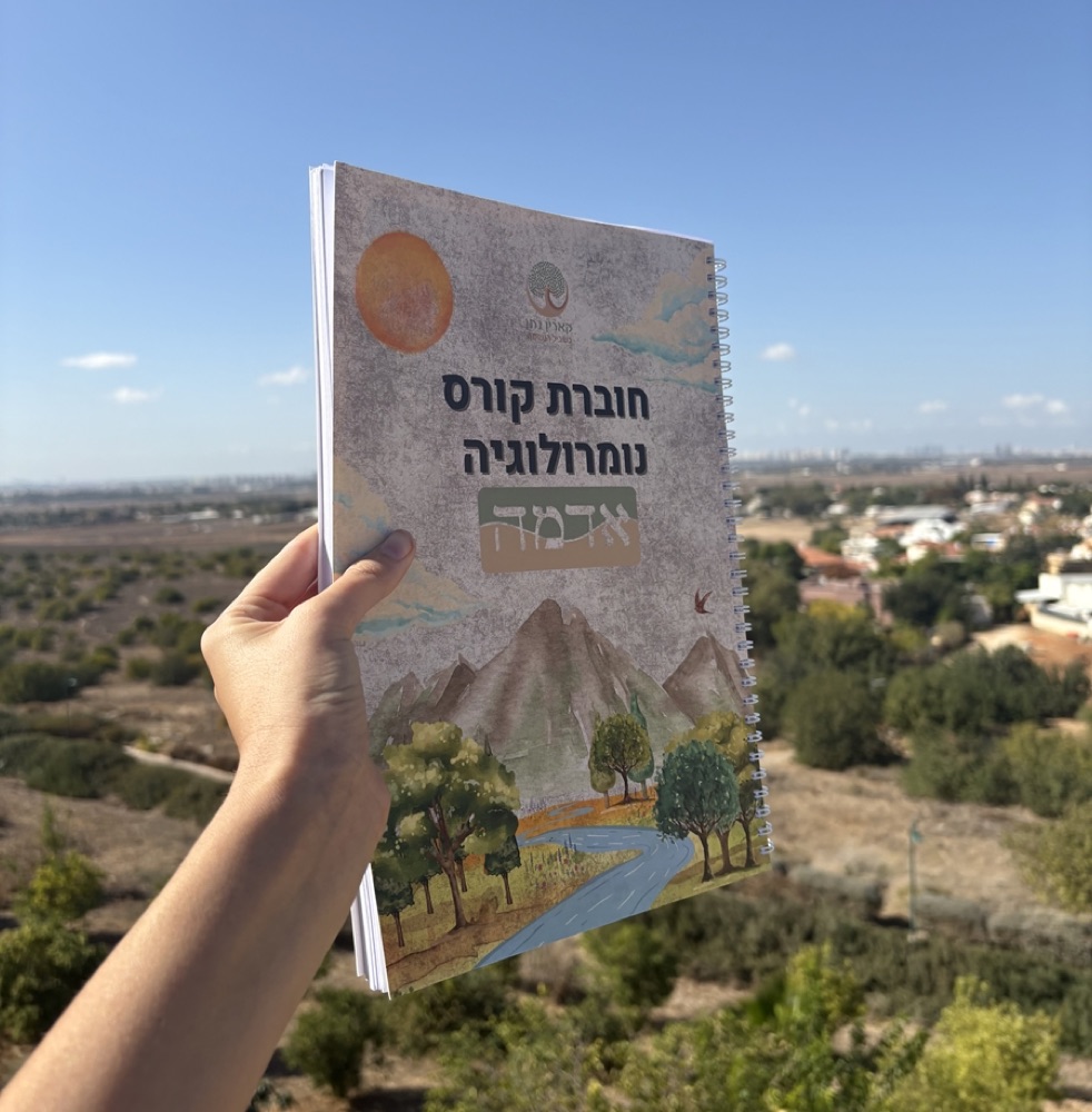 חוברת קורס נומרולוגיה אדמה מוחזקת ביד מול נוף